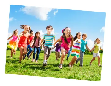 A group of smiling children run across a grassy field on a sunny day, holding hands. The sky is blue with a few clouds, and the kids appear happy and energetic.