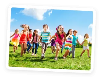 A group of smiling children, wearing colorful summer clothes, run together across a grassy field under a blue sky with scattered clouds.