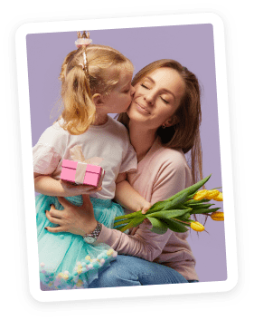 A young girl kisses a smiling woman on the cheek. The girl holds a pink gift box, and the woman holds a bouquet of yellow tulips. Both appear happy, set against a light purple background.